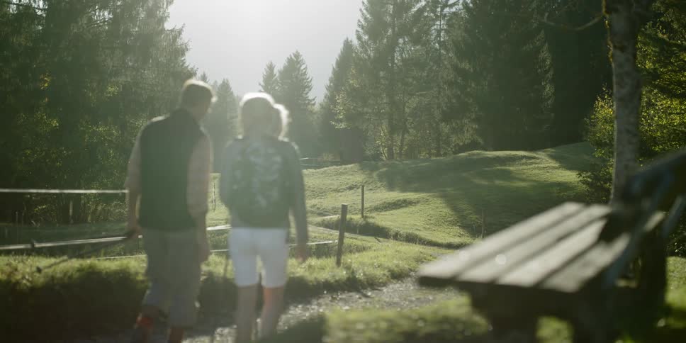Man and woman walk on a forest trail with walking sticks in their hands