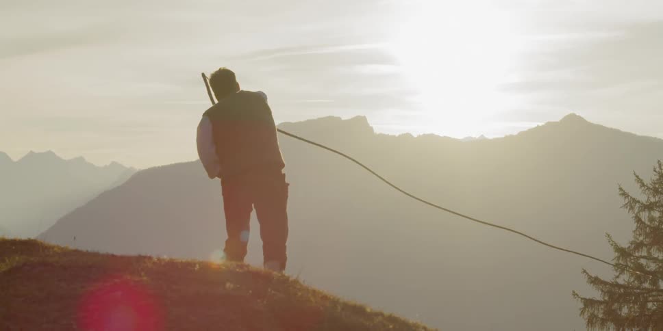Man swings whip on a hill while the sun goes down behind the mountains