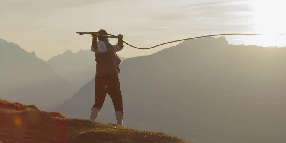 A man stands on a hill swinging a whip