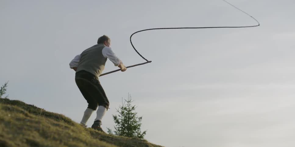 A caucasian male outside waving around a long rope on a stick