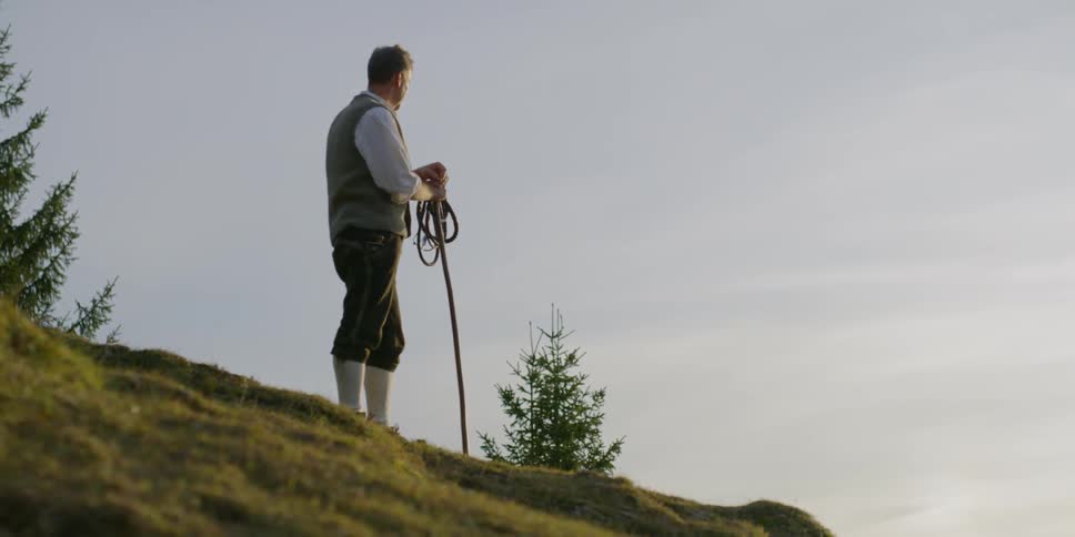 A male caucasian standing on a hill with a rope and a stick