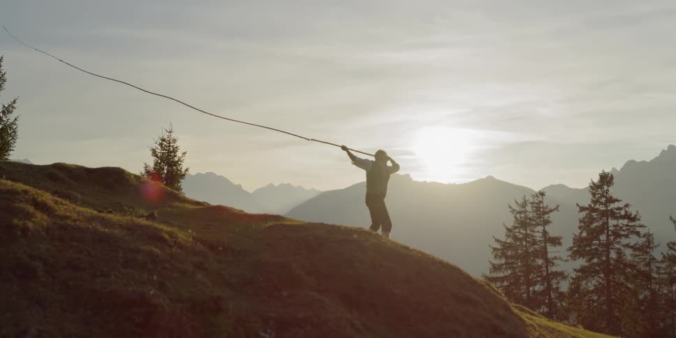 Man swings whip while the sun goes down behind the mountain