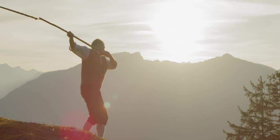 Man swings whip while the sun goes down behind the mountain