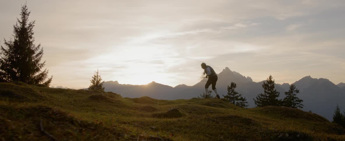 Man swings whip on a hill while the sun goes down behind the mountain