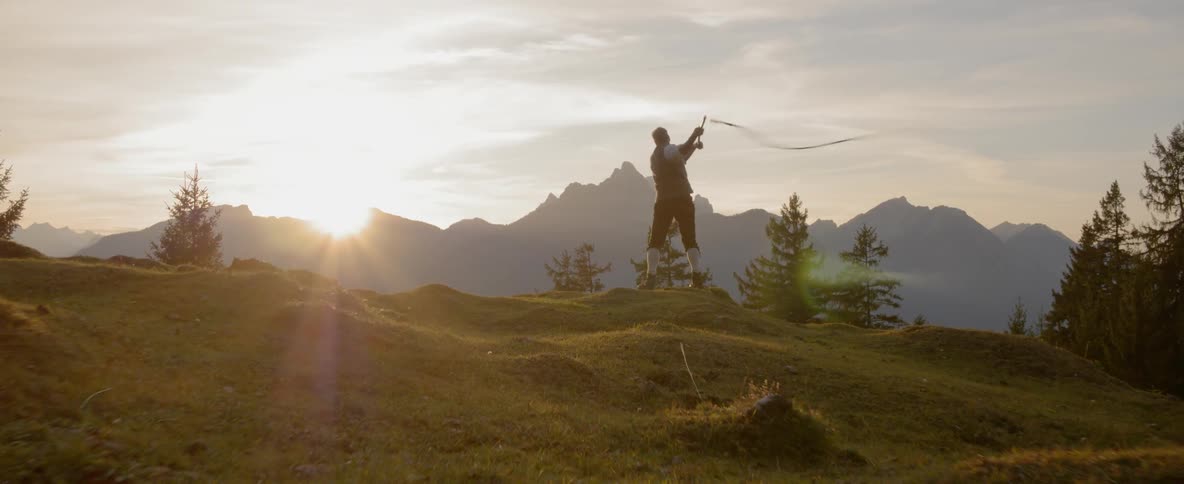Man swings whip on a hill at sunset