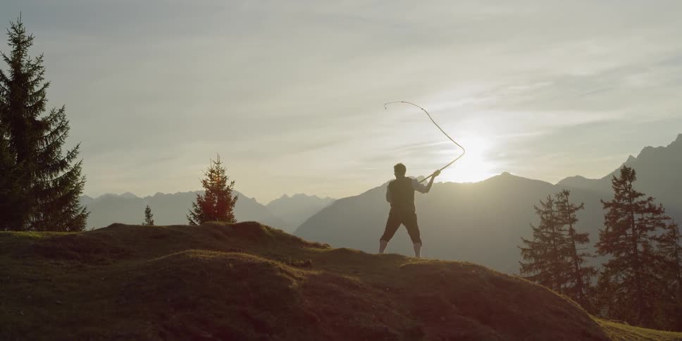 Man swings whip on a mountain at sunset