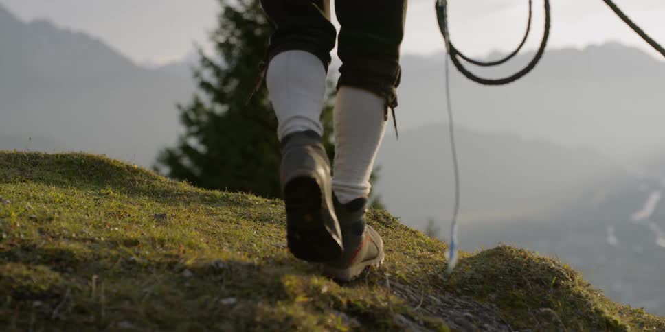 A man with a long whip casts it down a hillside