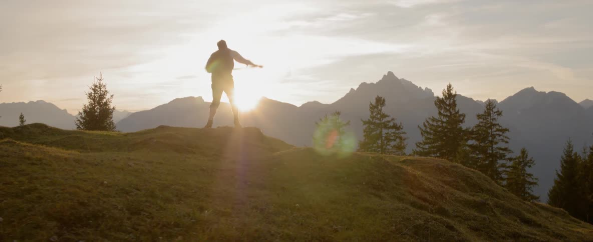 A white man aggressively swings a whip while standing on a hill