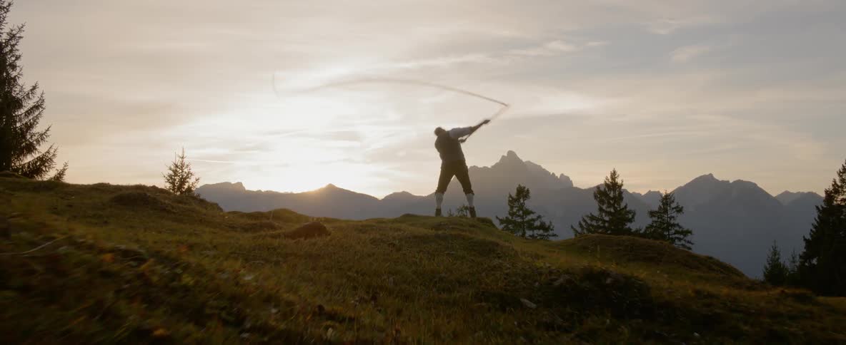 A man swings a whip while standing on a hillside