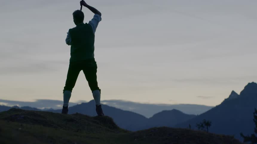 A man stands on a hill twirling a whip around himself