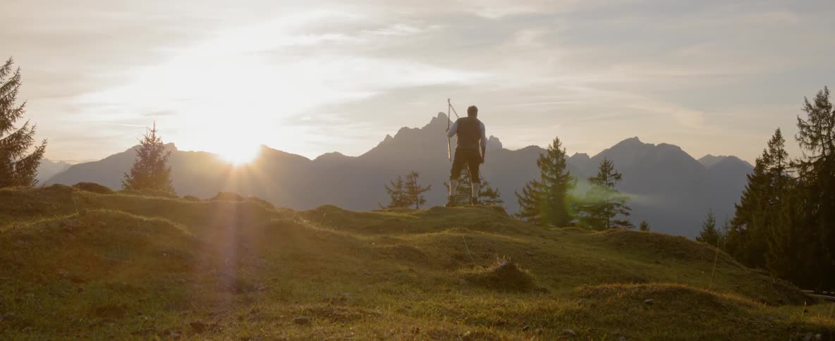 A man holds and swing a large whips around on top of a hill