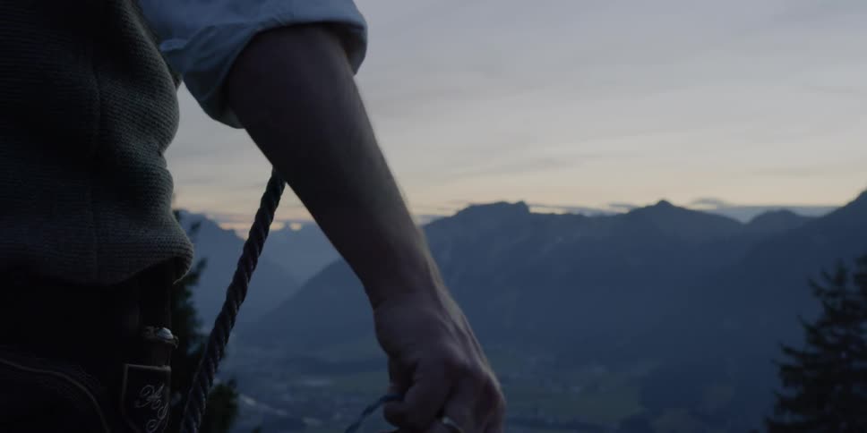 Man holds and swings whip with the landscape of mountains at dusk