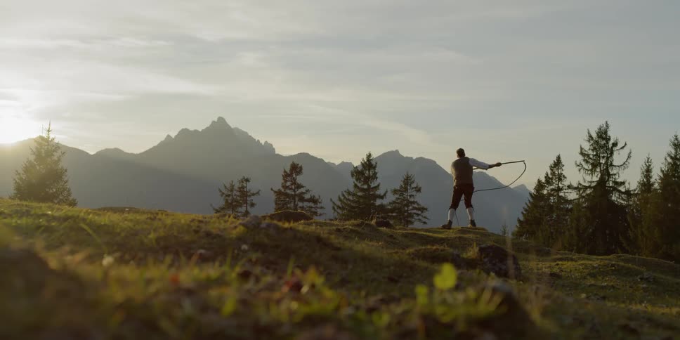 Man swings whip on a hill at sunset