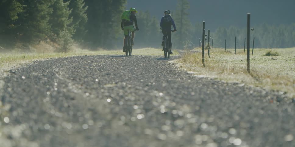 Two bicyclists ride on a rural gravel road on a sunny day