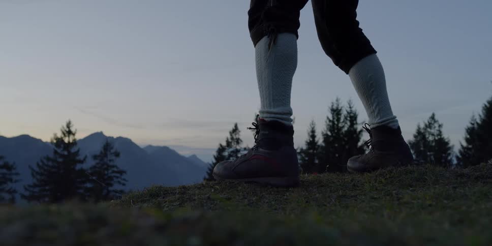 Man swings whip on a hill with the view of mountains at dusk
