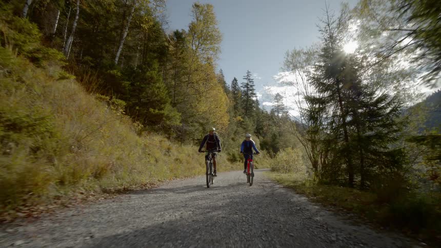 Two bicyclists approach on a gravel road and they almost catch up but far behind in the last moment