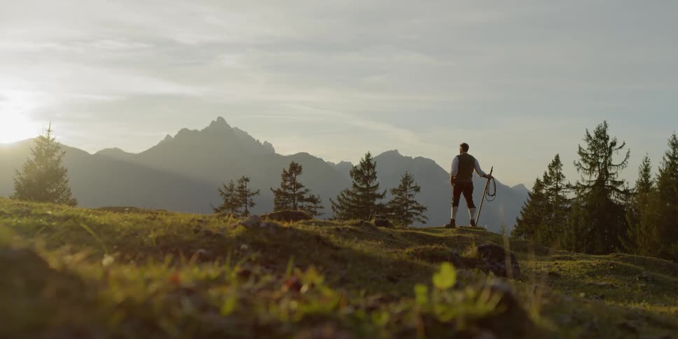A man standing in on hilly terrain gazing out at mountains in the distance