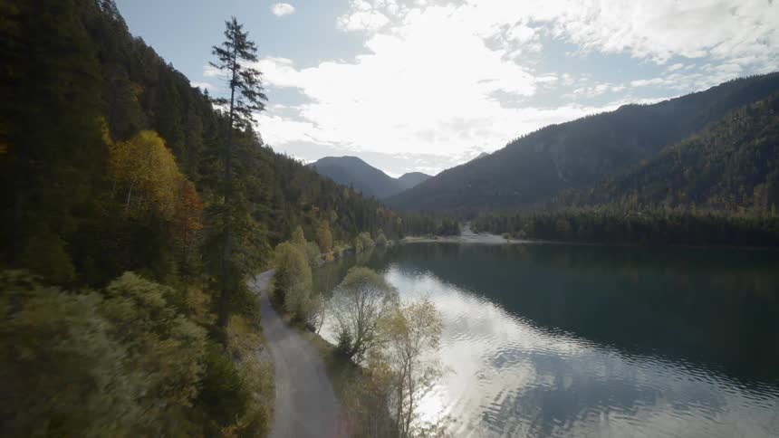 Two people bike down a road that winds by a calm body of water
