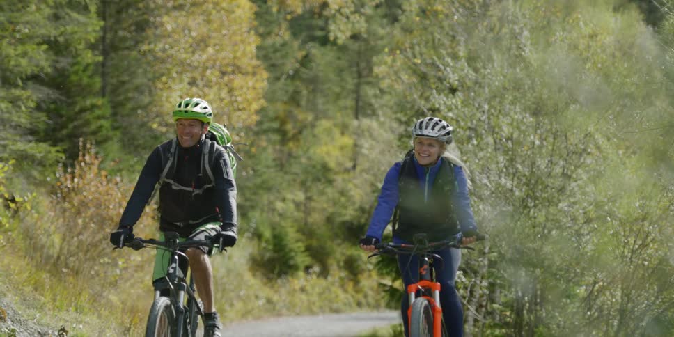 Couple riding bikes on a trail through the trees in the mountains
