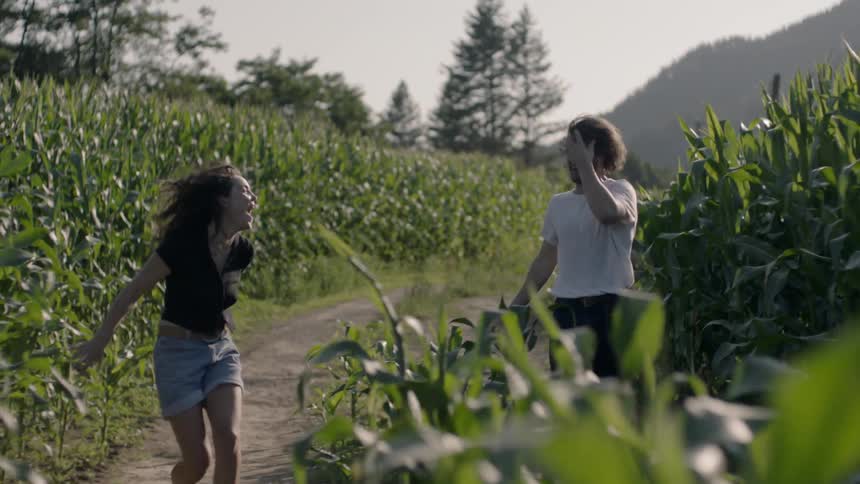 A man chases a woman through a corn field while they both laugh