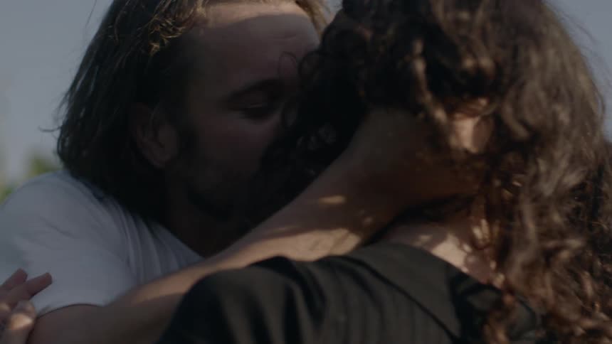 Man kisses woman in the field of corn while the sun shines behind the mountain
