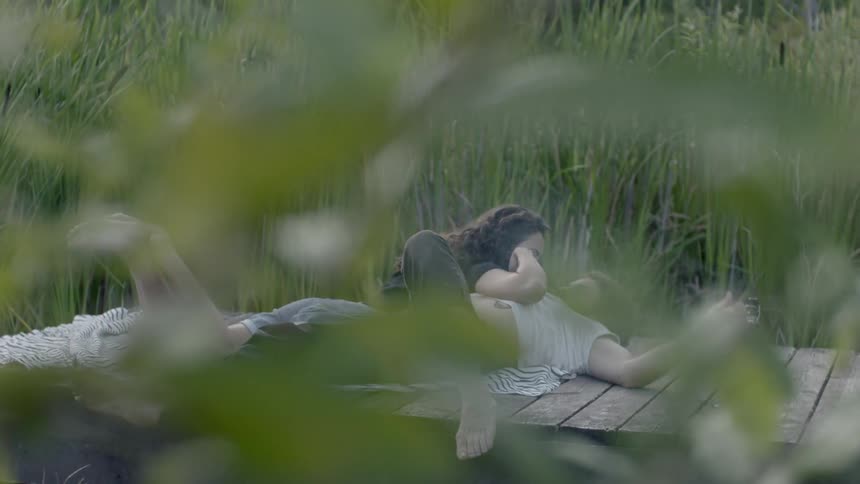 A woman lies together with a man on a wooden dock
