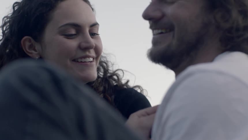A man and woman sit on the ground smiling and talking to each other