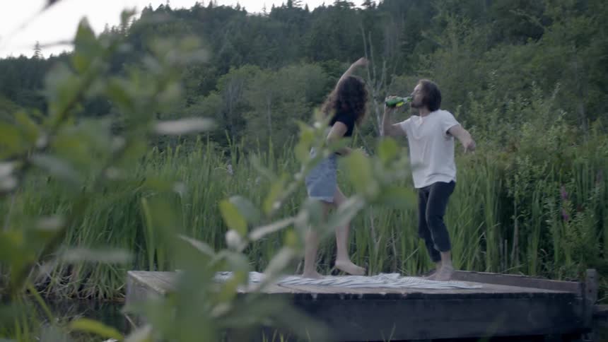 A man is drinking wildly on a dock by the lake