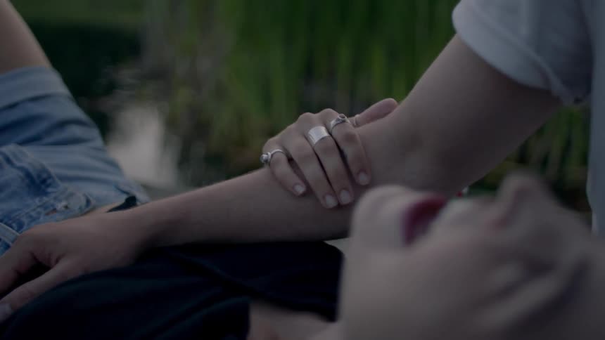 A man rests his arm on his girlfriends stomach as they sit near the water outdoors