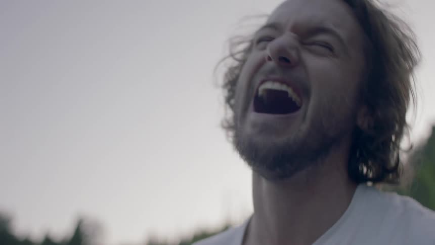 Woman puts her head on man's lap and laughs in the forest next to the lake at dusk