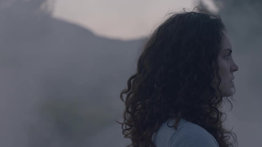 A woman stands in fog with her eyes closed until she opens them