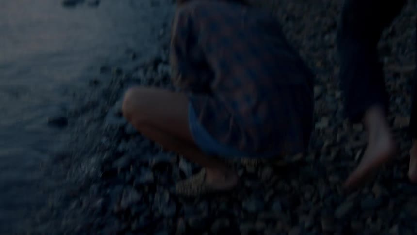 A man and woman pick up rocks on a rocky shore at sunset then hug each other