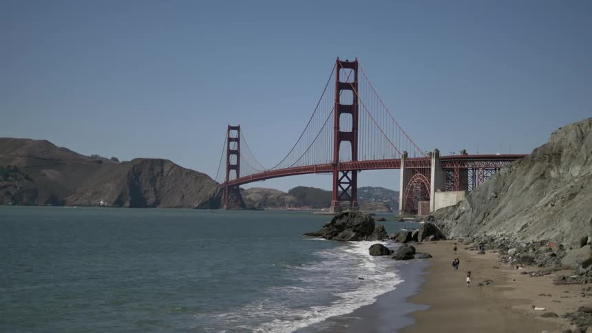 People walking along the shoreline near a bridge