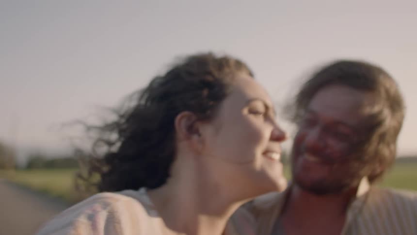 Man and woman sitting in a driving roadster car hug and laugh at sunset