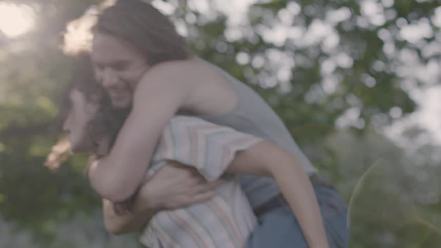 Woman carries man over her shoulders in the forest on a sunny day