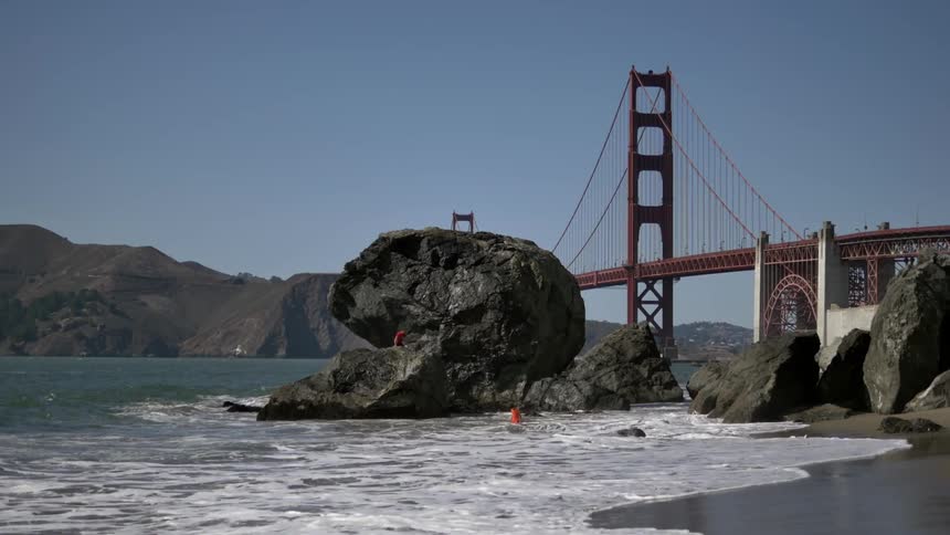Water crashes on the beach with the golden gate bridge in the background