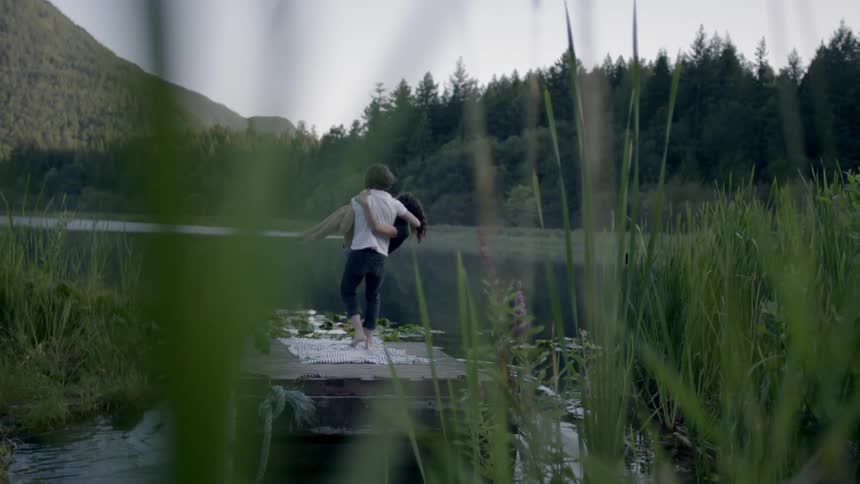 A man picks up a woman off of a dock