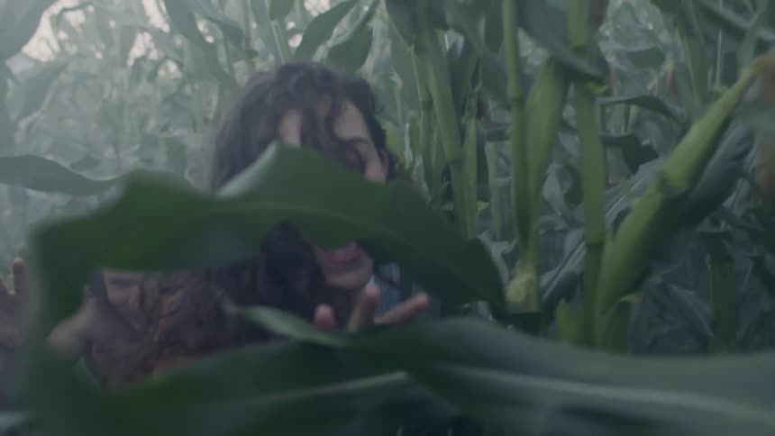 A man and a woman running through a field of tall crops