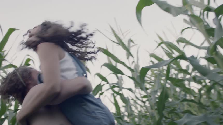 Shirtless man hugs woman in the field of corn in the daytime