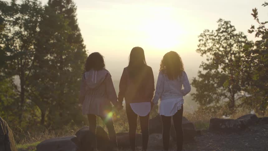 Three women hold hands on the cliff edge