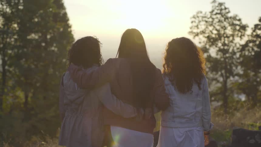 Three women stand on a hill looking out over a valley