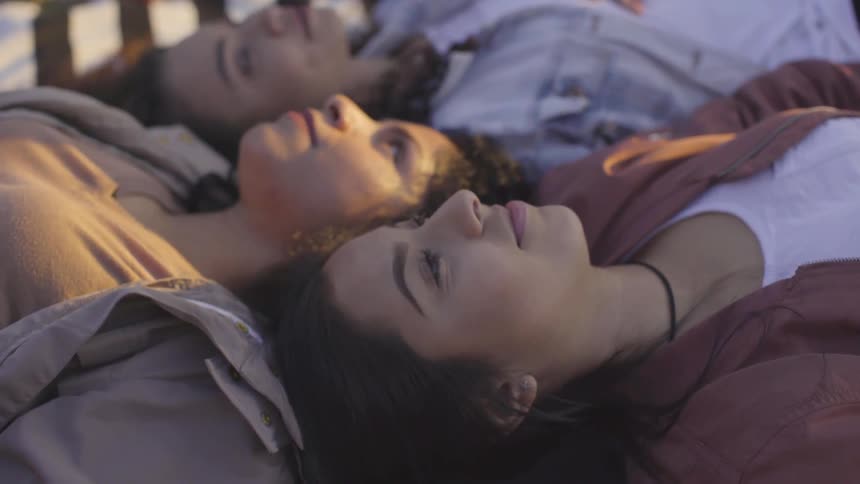 Three young women talking while lying outdoors on a striped blanket