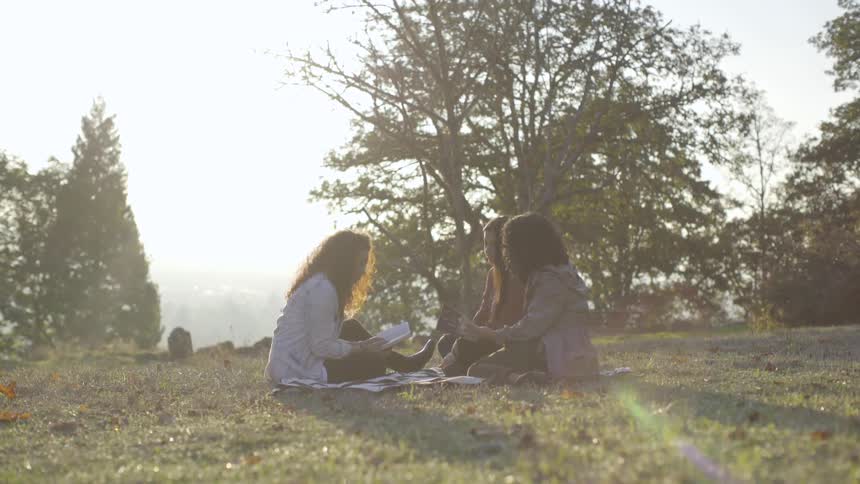 Three friends sit on a blanket together in the grass