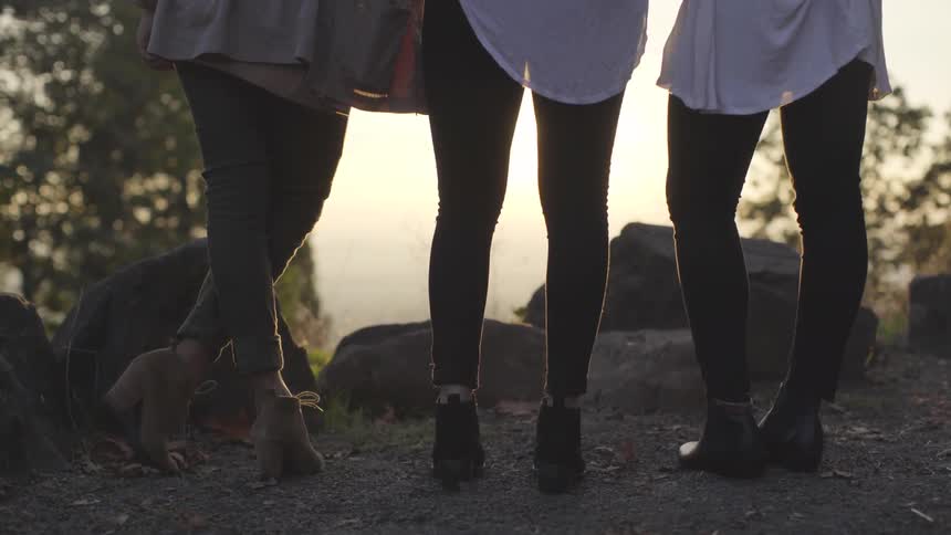 The legs of three girl friends as they stand on a ridge at sunset