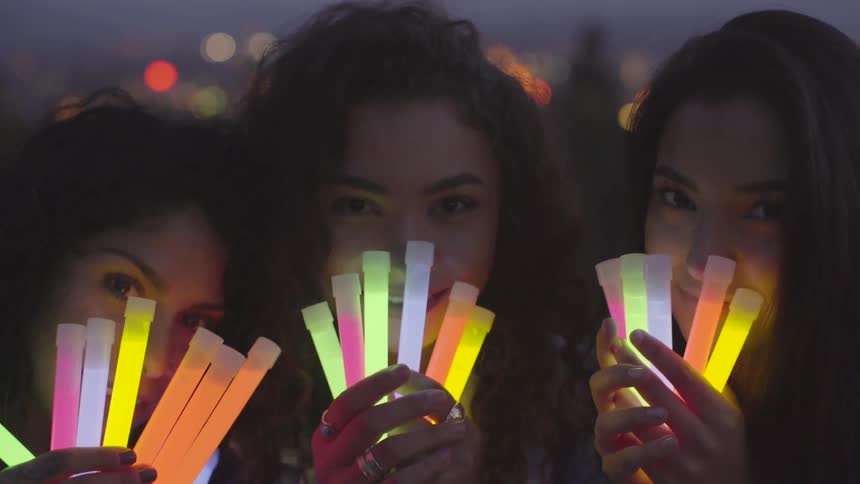 Three women hold glowsticks in front of their faces