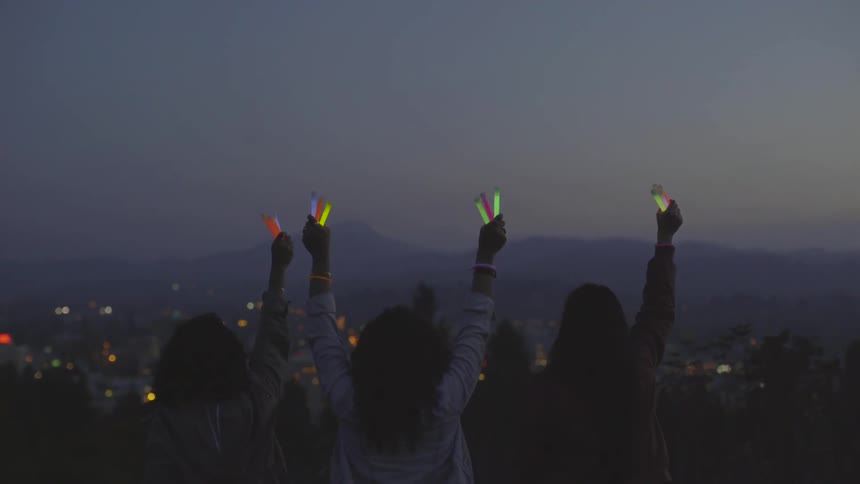 Three young woman thrust glow sticks up into the air