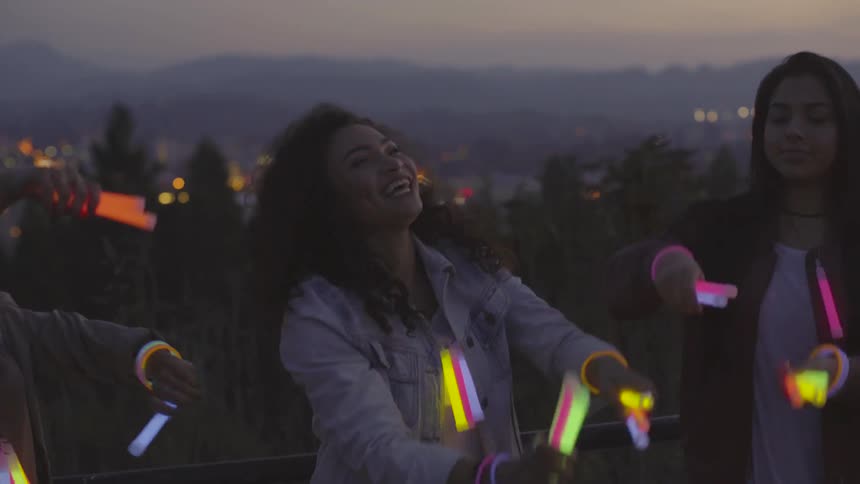 A group of women dancing with glow sticks outdoors in the evening
