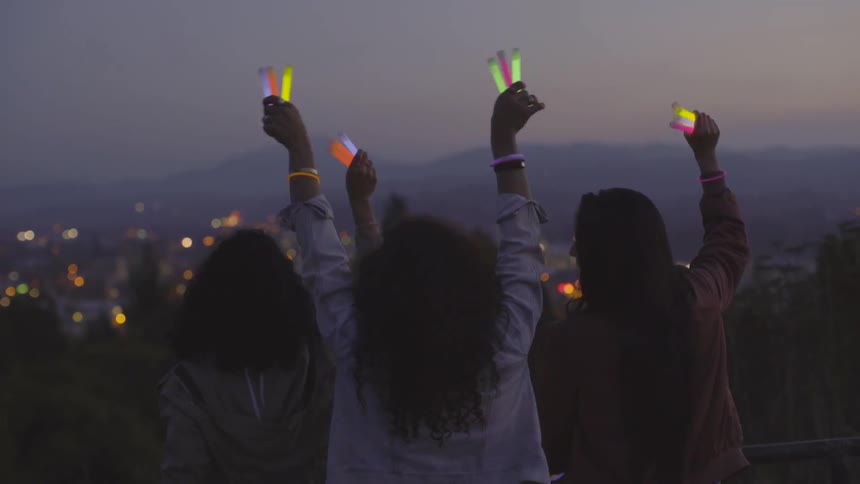 Three girls stand outside waving glow sticks in the air