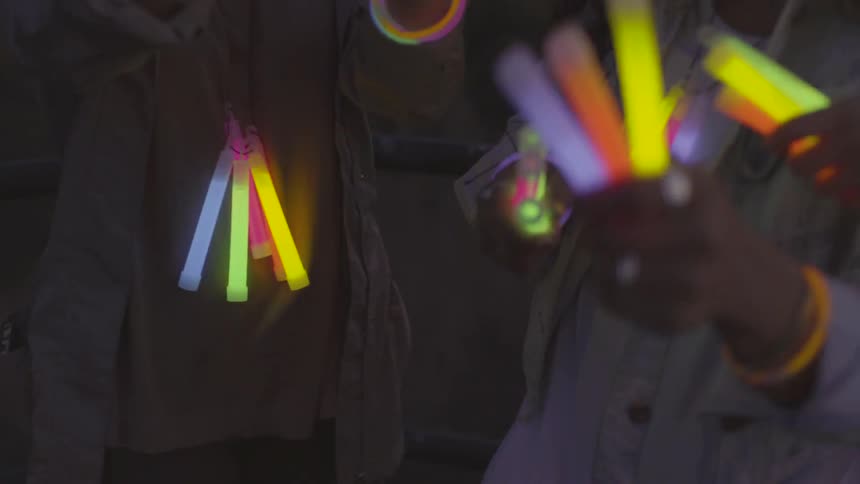 A group of women in a dark location dancing with glow sticks and glowing bracelets