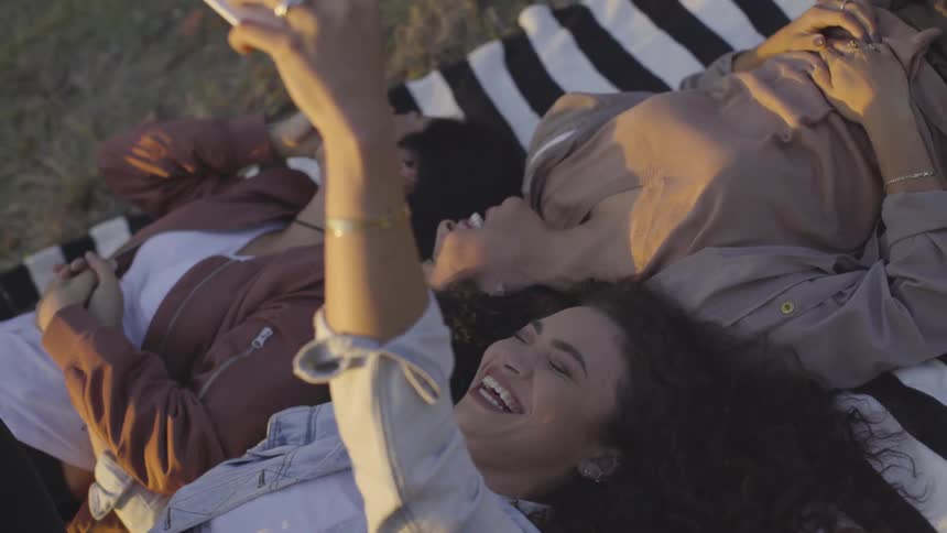 Three young women lying on a blanket laughing and taking a selfie